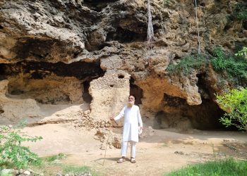 A tourist guide standing infront of the Buddha Caves with a shaft in his hand.