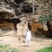 A tourist guide standing infront of the Buddha Caves with a shaft in his hand.